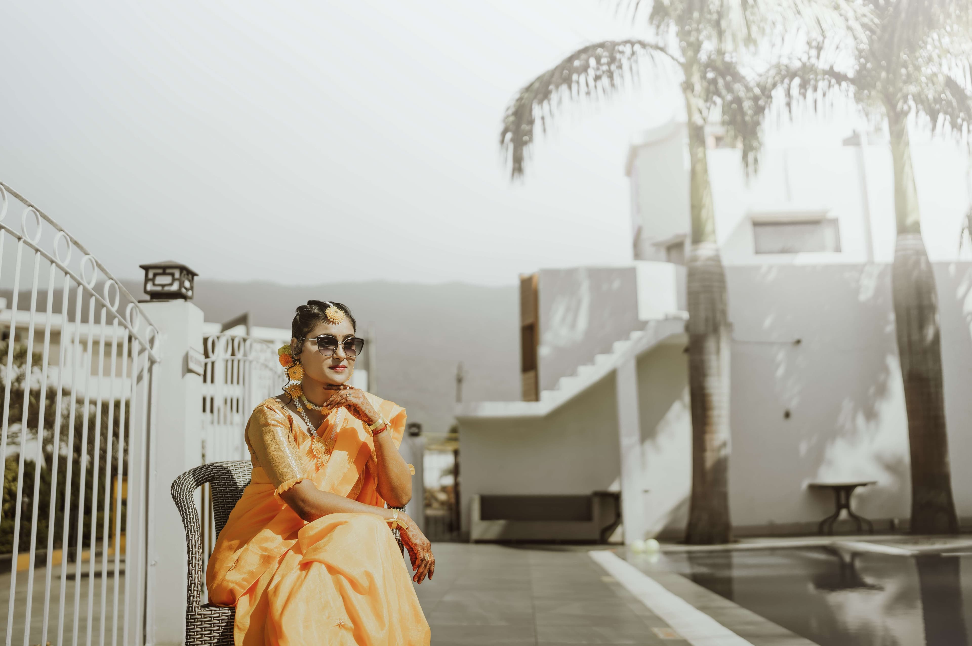 A woman in an orange sari enjoys a peaceful moment on a chair by the pool, beautifully captured in a candid photograph