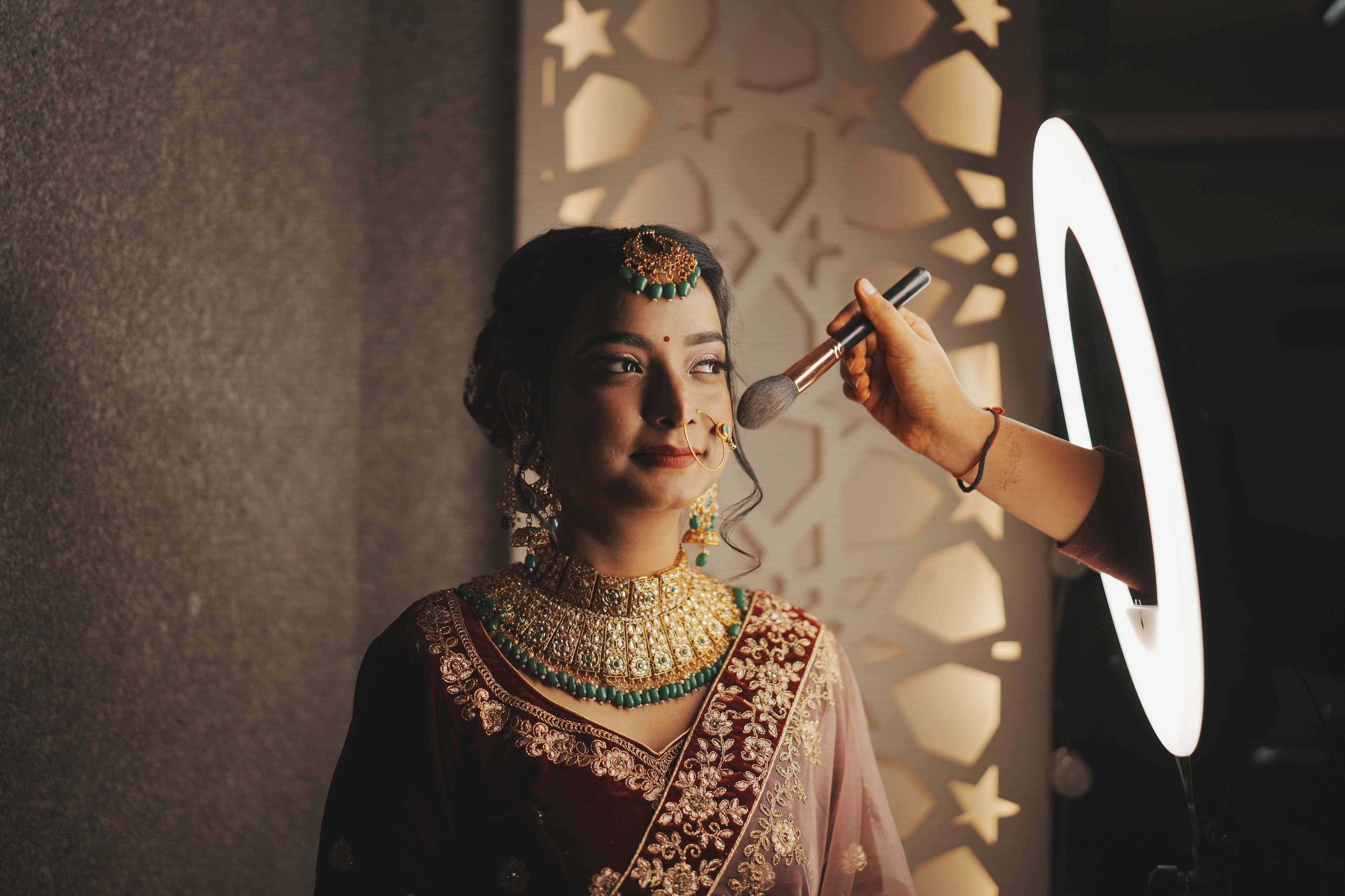 A woman in vibrant traditional Indian attire smiles as she prepares for her wedding, captured in a candid moment of joy